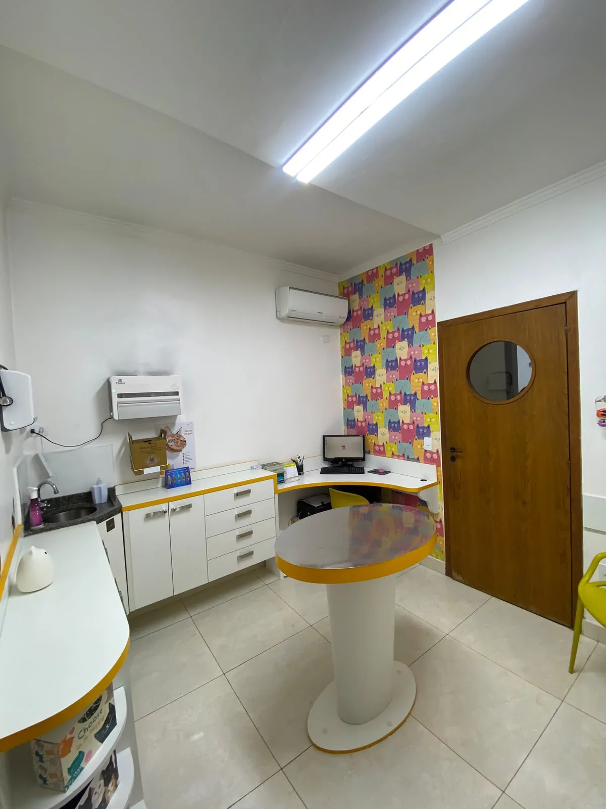 Consultório dos felinos com bancada, pia, papel de parede de gatos e mesa de atendimento redonda