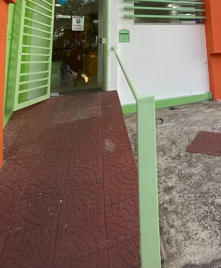 Entrada do Centro Veterinário Guarani vista da calçada, com o portão verde aberto, a rampa de acesso com corrimão e a área recuada em frente à casa