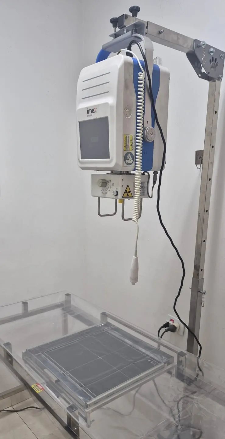 Aparelho de radiografia digital da clínica: o gerador de raio X, com o símbolo de radiação, suspenso num suporte de metal sobre a mesa de exame transparente